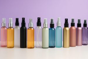Variedad de envases cosméticos tipo body mist sin etiquetas en vidrio, PET y aluminio sobre fondo corporativo Bull Estética en tonos lila y blanco, estética premium y profesional.
